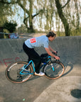 Cyclist in skate park wears The Handmade Cyclist Dossard 13 T-shirt in pale blue.