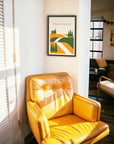 Yellow armchair in a room with a framed poster of Strade Bianchi on the wall, designed by the Handmade Cyclist