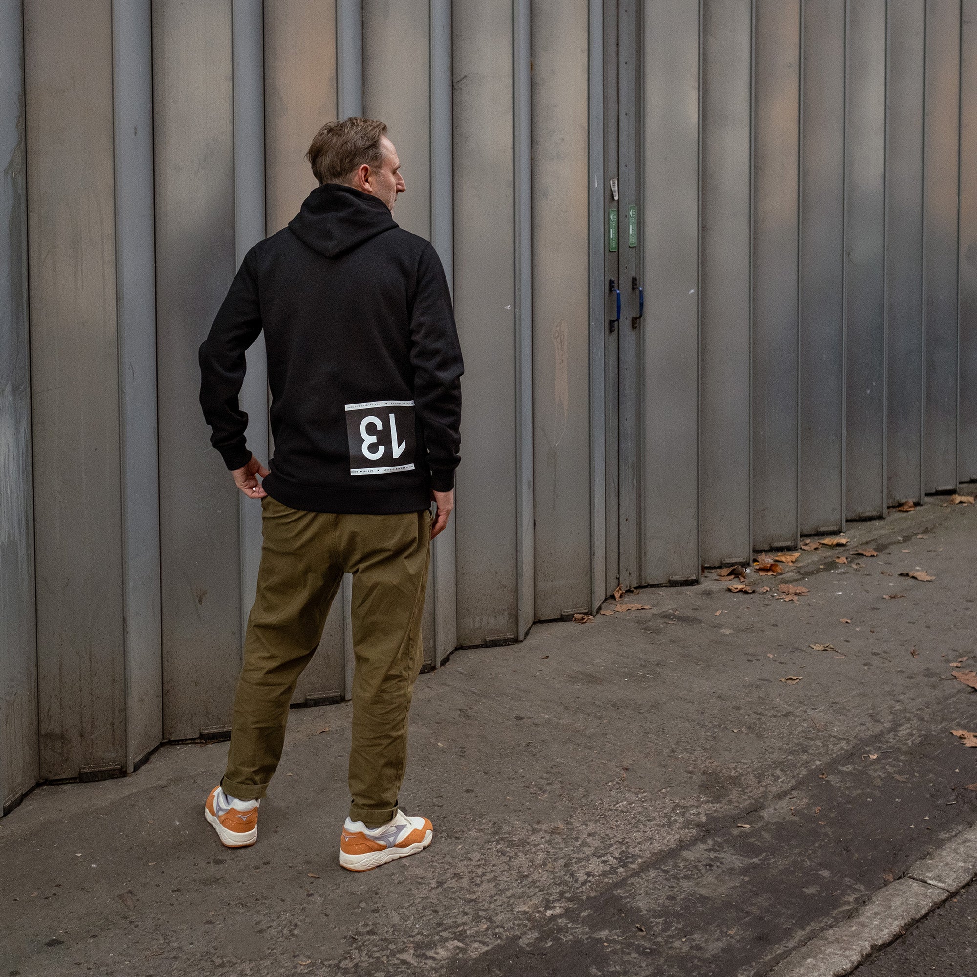 Man wearing a black hoodie with a cycling race-number style upside 13 print on rear.