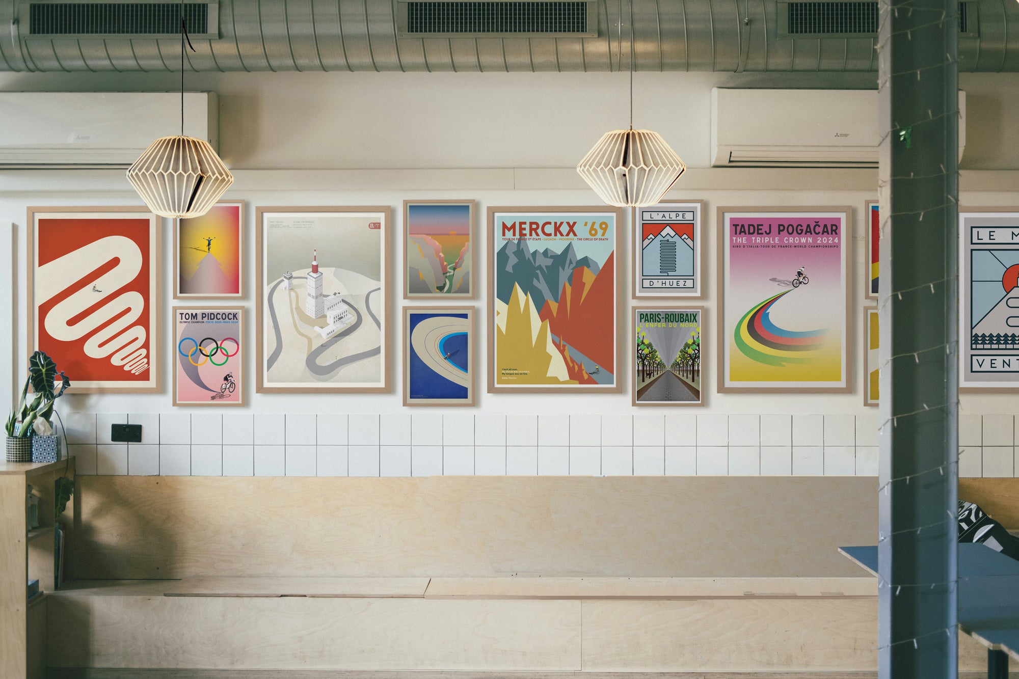 Colorful cycling-themed posters and artworks hanging on a tiled wall in a modern interior setting, designed by The Handmade Cyclist.