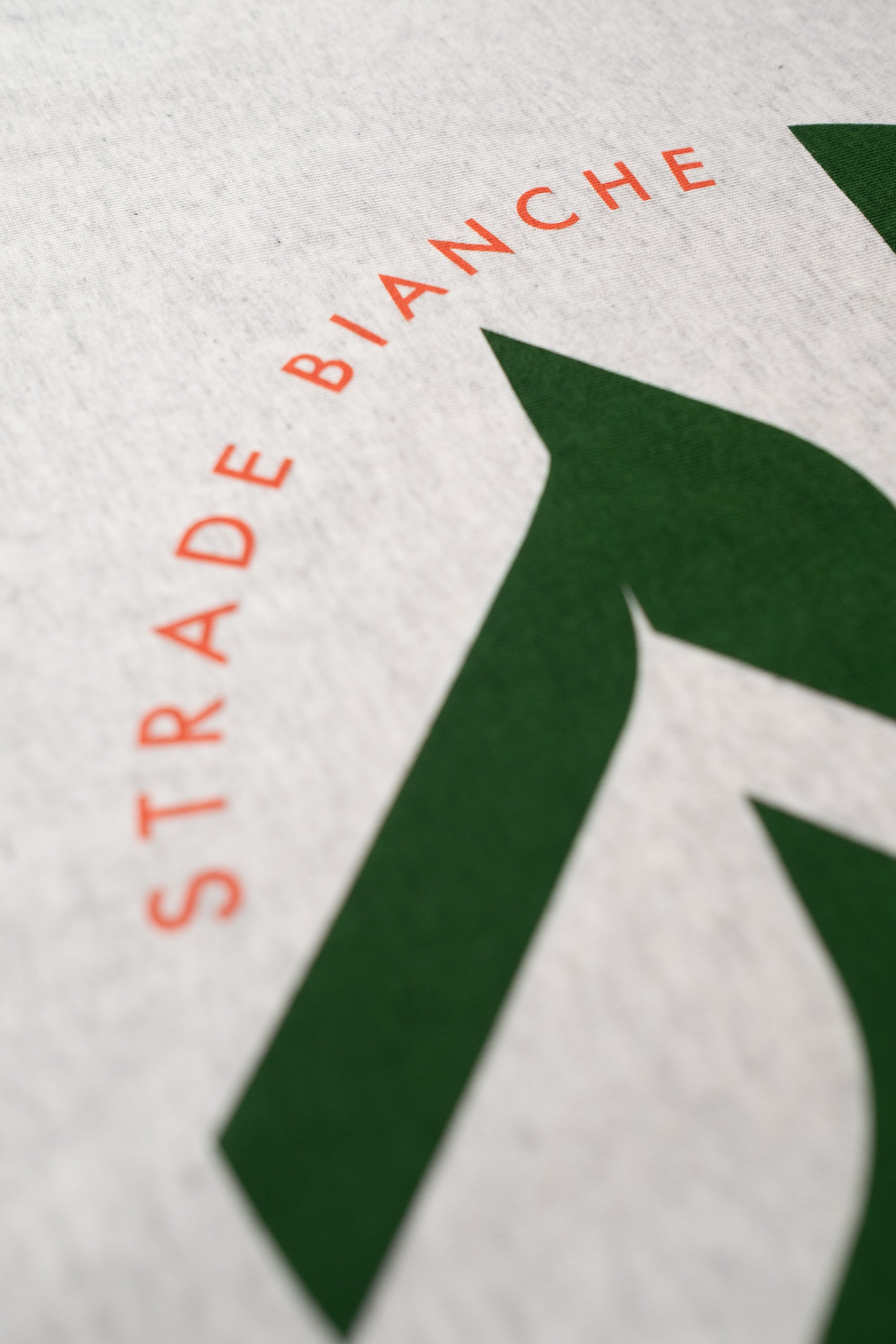 Close-up of a white t-shirt with a green print featuring Strade Bianchi design by The Handmade cyclist.