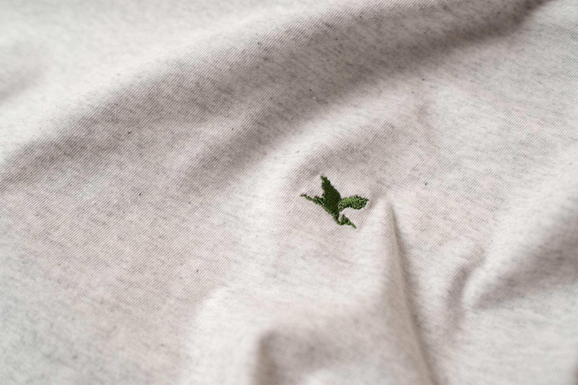 Close-up of a white t-shirt with a green embroidered Heron logo. Design by The Handmade cyclist.