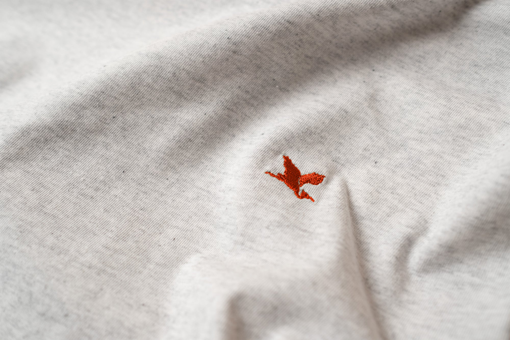 Close-up of a red embroidered Heron logo on a white t-shirt, by the Handmade Cyclist.