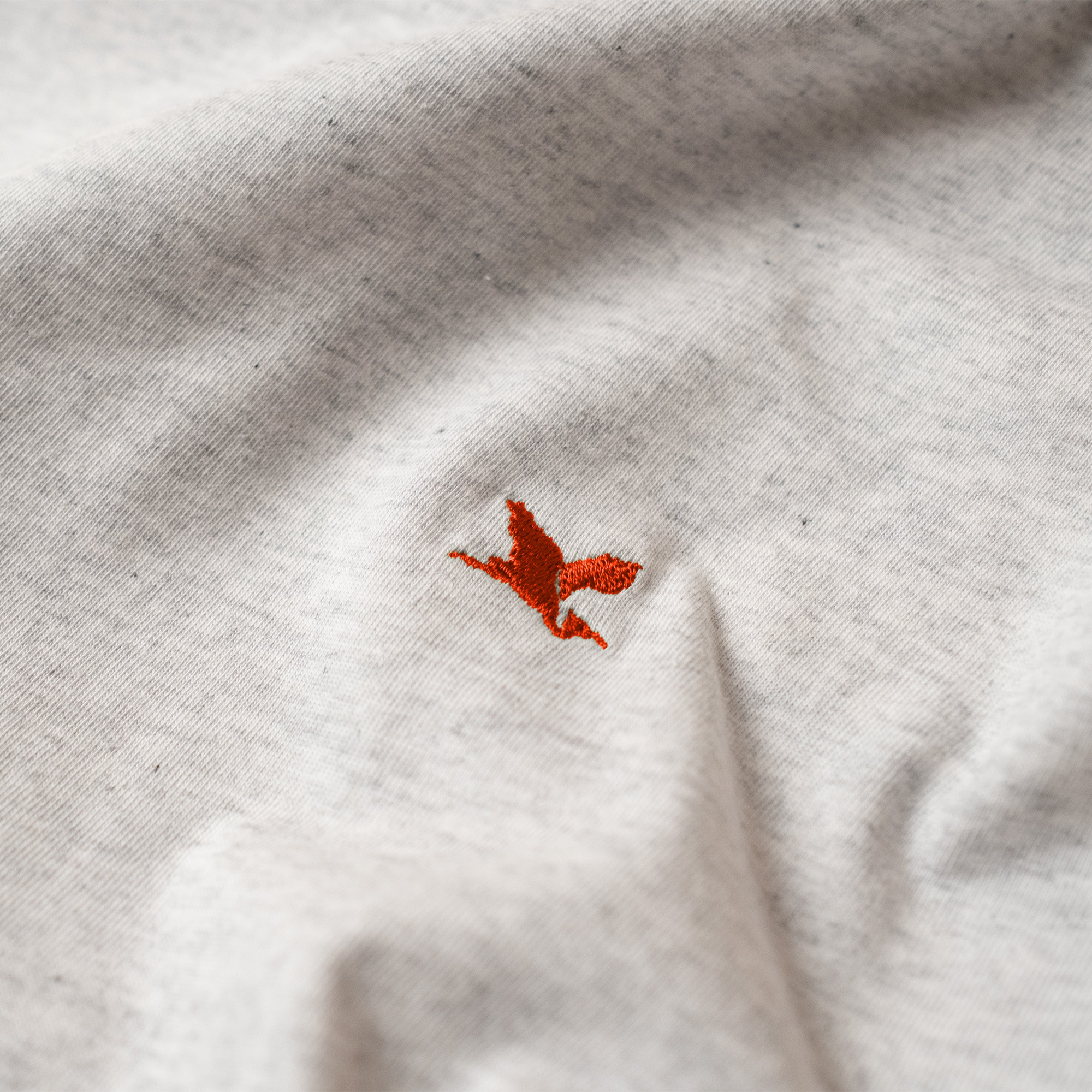 Close-up of a white t-shirt with a red embroidered Heron emblem. The Handmade Cyclist.
