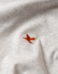 Close-up of a white t-shirt with a red embroidered Heron emblem. The Handmade Cyclist.