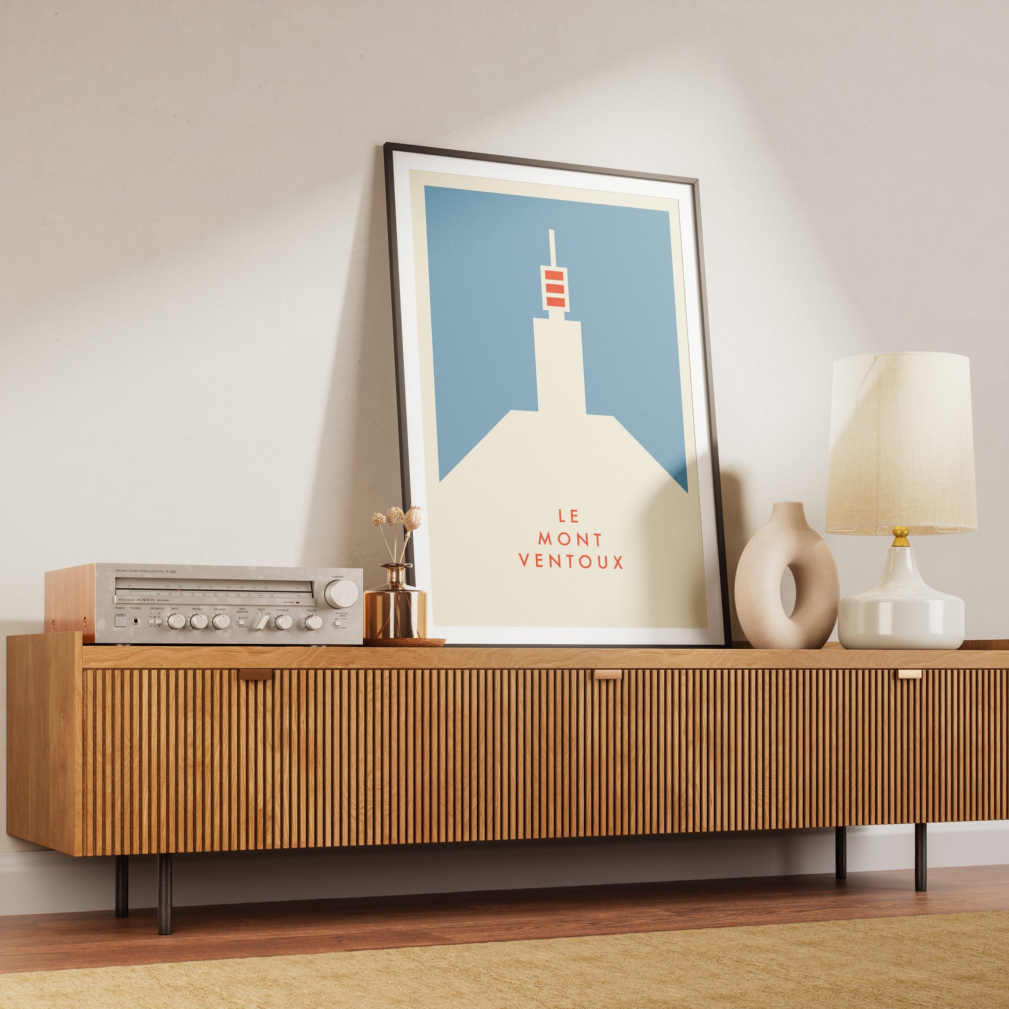 Wooden sideboard with a lamp, vase, and framed cycling art print of Le Mont Ventoux by Handmade Cyclist in a black frame.